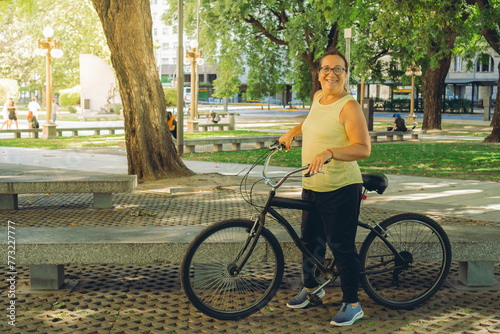 happy middle-aged latin woman standing next to her bike in a park smiling with vitality. copy space