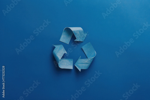 A metallic  three-arrow recycling symbol lies centered on a vibrant blue backdrop  indicative of environmental themes