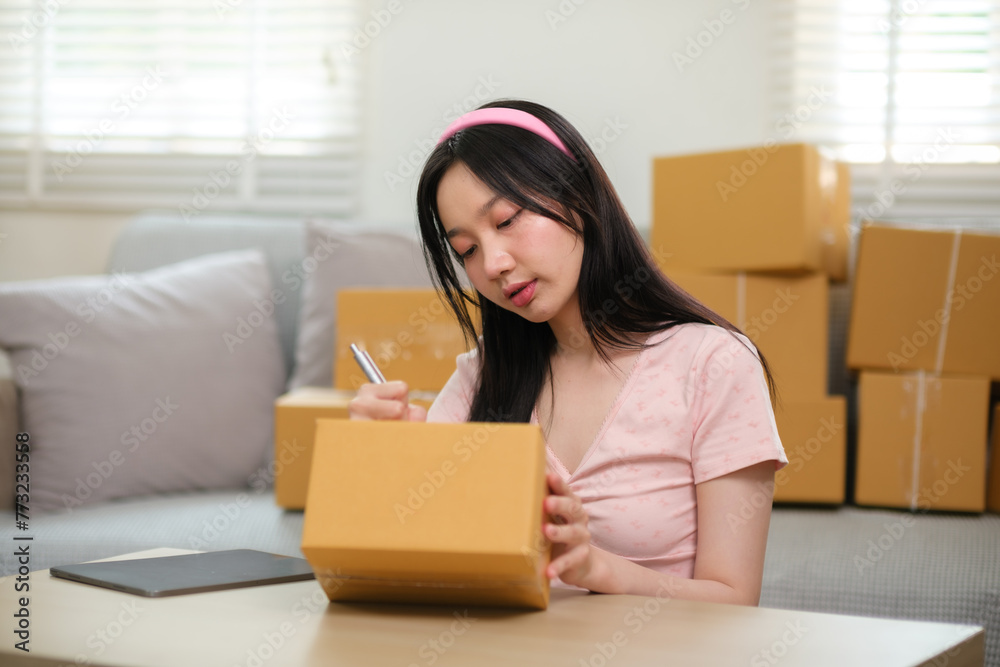 Startup small business owner working at home, woman writing address on parcel box at home for delivery order to customer, Online shopping business, ecommerce concept Startup small business owner working at home, woman writing address on parcel box at home for delivery order to customer, Online shopping business, ecommerce concept