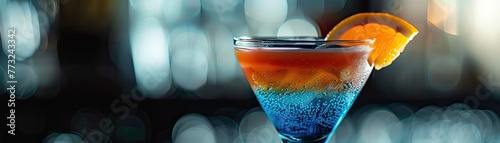 A close-up of a cocktail with blue and orange layers served in an elegant glass