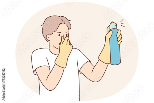 Dissatisfied man with spray to remove unpleasant odors covers nose with hand spraying freshener