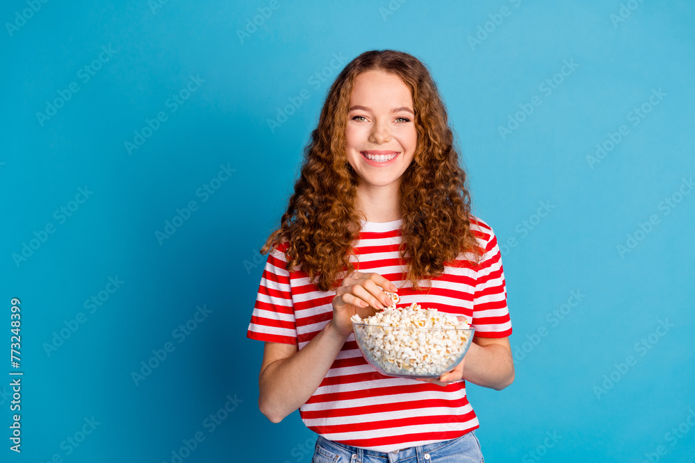 Photo of positive optimistic woman with wavy hairdo dressed striped t-shirt eat popcorn at cinema isolated on blue color background