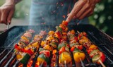 close-up of hands grilling colorful vegetables and skewers over a charcoal barbecue, smoke rising in the summer