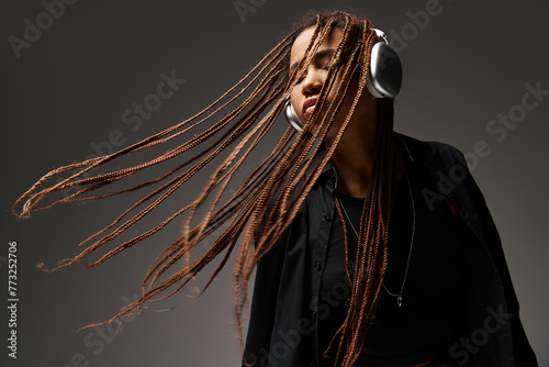 ecstatic dance of carefree african american girl with dreadlocks and wireless headphones on grey