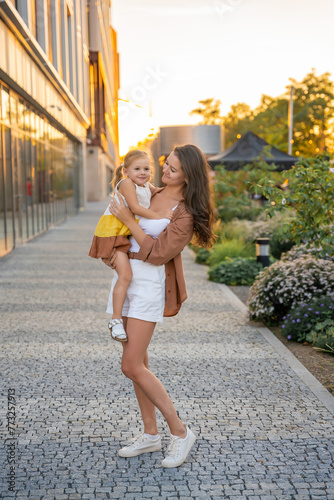 Mom and her little daughter playing on city street at sunset lights in summer