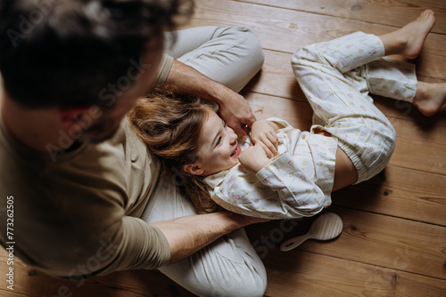 Φωτογραφία Top view of father with daughter on floor laughing together, having fun, tickling each other