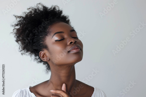 Photo of a beautiful African American woman inhaling air with her eyes closed against a light background.