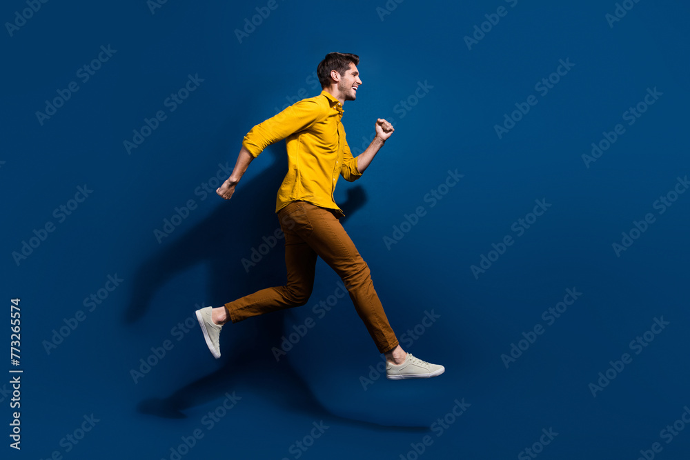 Full body photo of handsome young guy jump running hurry shopping dressed stylish yellow outfit isolated on dark blue color background Full body photo of handsome young guy jump running hurry shopping dressed stylish yellow outfit isolated on dark blue color background