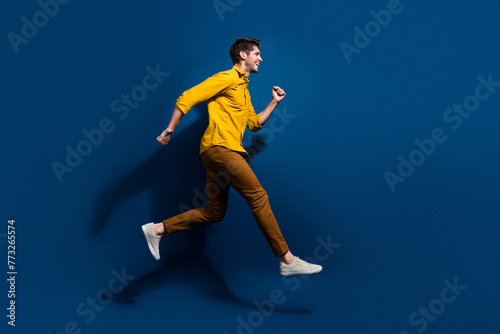 Full body photo of handsome young guy jump running hurry shopping dressed stylish yellow outfit isolated on dark blue color background © deagreez