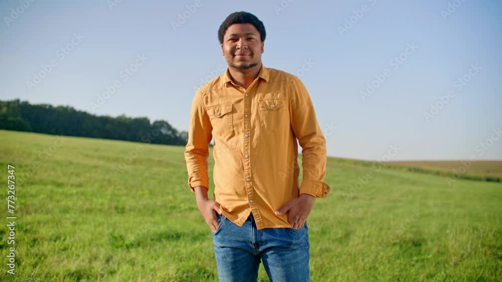 African American male with small beard standing in open field with green grass. Wearing jeans and orange shirt. Smiling while looking directly at camera. Blue sky without clouds in background. African American male with small beard standing in open field with green grass. Wearing jeans and orange shirt. Smiling while looking directly at camera. Blue sky without clouds in background.