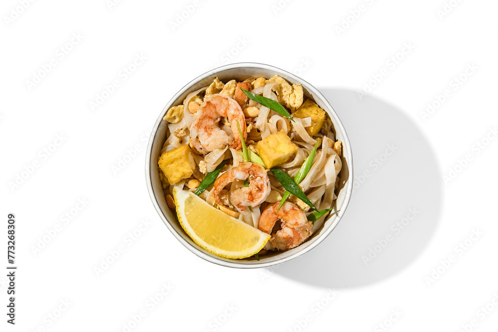 Traditional asian street food - pad thai noodles with shrimp, vegetables and tofu isolated on white background. Pad thai udon with prawns and lemon in ceramic bowl. Fried udon noodles with seafood. Traditional asian street food - pad thai noodles with shrimp, vegetables and tofu isolated on white background. Pad thai udon with prawns and lemon in ceramic bowl. Fried udon noodles with seafood.