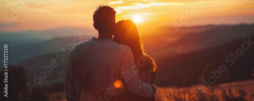 Back view of a romantic couple embracing as they watch a serene sunset over a scenic landscape.