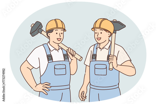 Men in builders uniforms and hardhats hold sledgehammers to demolish wall of emergency building