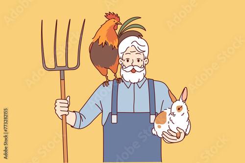Elderly man farmer engaged in agriculture and livestock raising holds rake and rabbit with rooster. Happy grandfather farmer rejoices at having own farm and possibility of country life