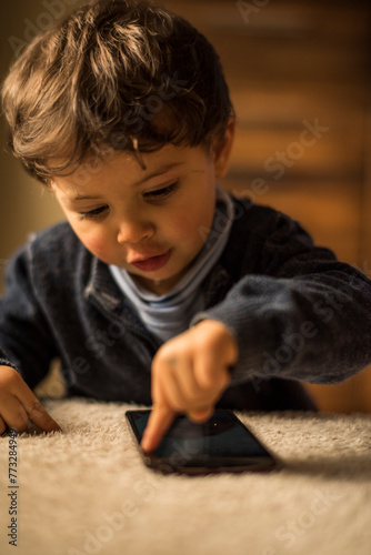 Baby one year old boy touching smartphone at home living room.