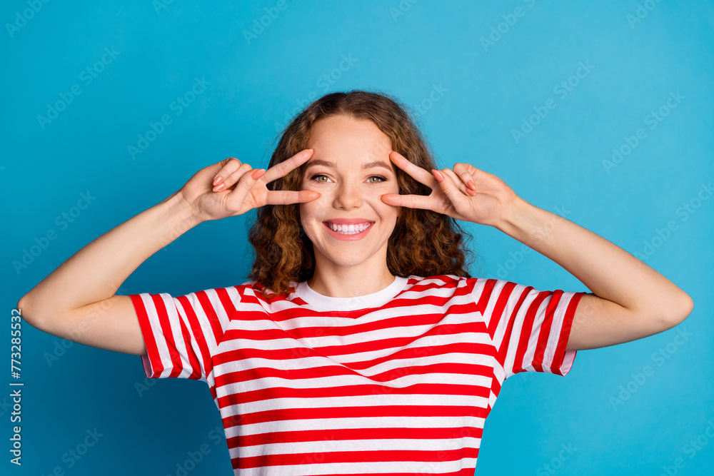 Photo of pleasant funky cute woman with wavy hairstyle dressed striped t-shirt show v-sign on eyes isolated on blue color background Photo of pleasant funky cute woman with wavy hairstyle dressed striped t-shirt show v-sign on eyes isolated on blue color background