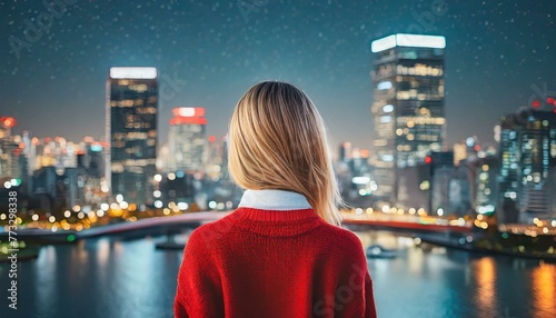 Woman with blonde hair and red sweater looking at a brightly lit city.
