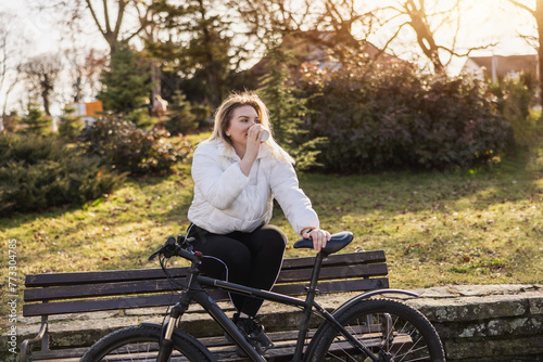Woman Enjoying a Coffee on a Park Bench With Bicycle During Golden Hour