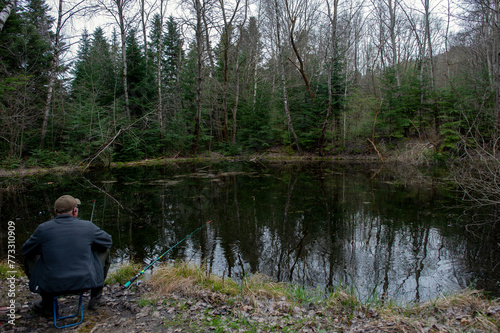 a fisherman on the shore of a pond pulls a spinning fish on a cloudy day