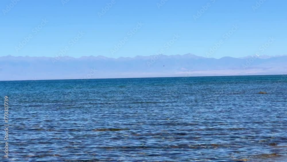 View of Issyk-Kul mountain lake, Kyrgyzstan. Waves splash on a sandy beach with rocks. Calm, peaceful natural background. Lake with a view of the Tien Shan Mountains. Kyrgyzstan 4K