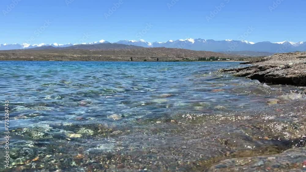 View of Issyk-Kul mountain lake, Kyrgyzstan. Waves splash on a sandy beach with rocks. Calm, peaceful natural background. Lake with a view of the Tien Shan Mountains. Kyrgyzstan 4K View of Issyk-Kul mountain lake, Kyrgyzstan. Waves splash on a sandy beach with rocks. Calm, peaceful natural background. Lake with a view of the Tien Shan Mountains. Kyrgyzstan 4K