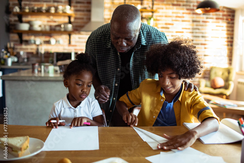 Father helping children with homework at kitchen table photo