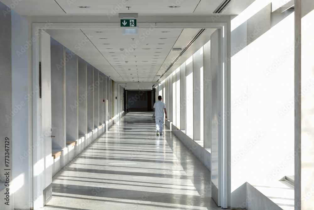 A medical worker walks along a long white corridor in a hospital