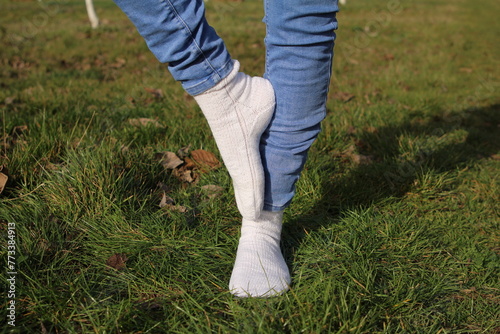 A person's legs in jeans and white boots walking on grass