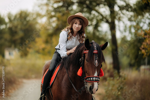 A girl in a white shirt and hat sits on a beautiful brown horse.