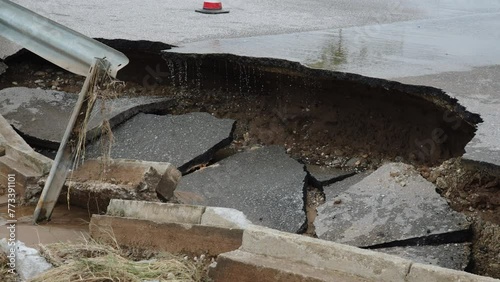 Closeup of destroyed edge of highway due to soil erosion. Water drips from road after rainstorm, pieces of broken asphalt lie with concrete pieces of curb. Bicycle passes along road.