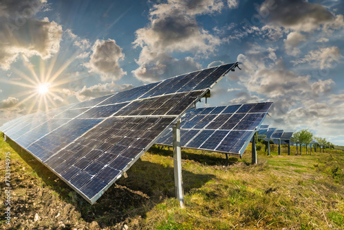 Rows of solar panels are soaking up sunlight in a lush green field with a few clouds adorning a blue sky above.
