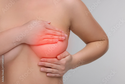Naked young woman suffering from breast pain on light grey background, closeup