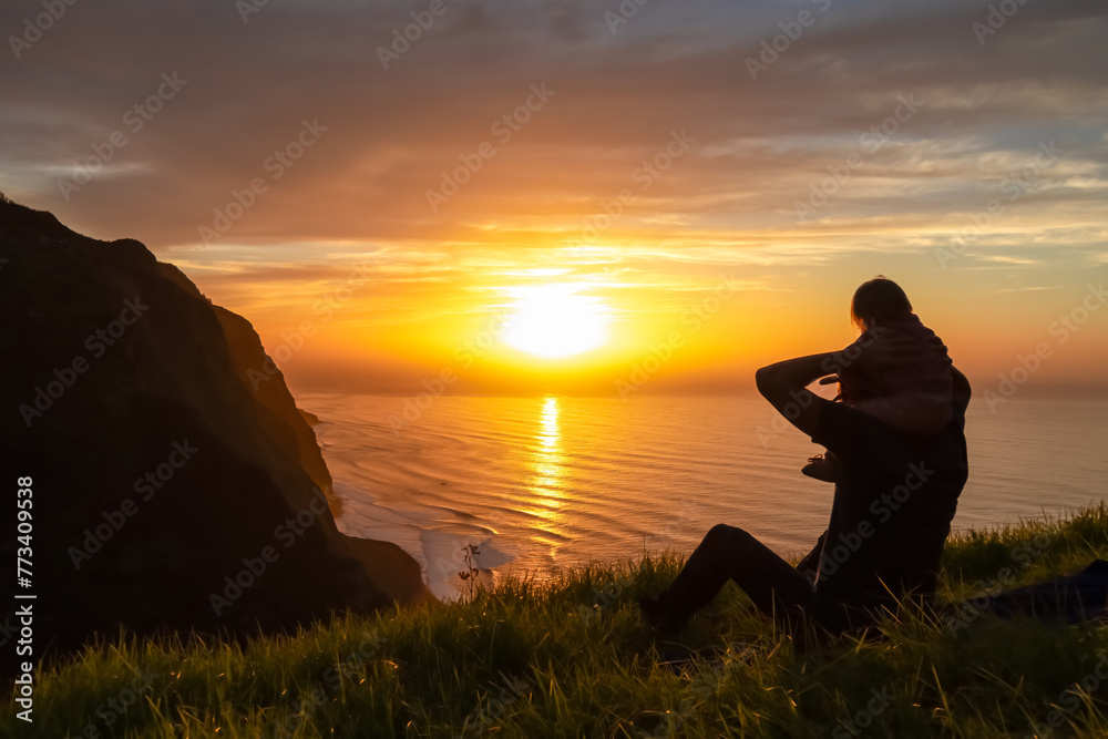 Toddler on shoulder of father on meadow with breathtaking sunset at viewing point Miradouro do Ponta da Ladeira, Madeira island, Portugal, Europe. Panoramic view of majestic coastline Atlantic Ocean