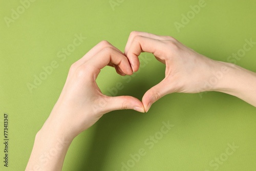 Woman showing heart gesture with hands on green background  closeup