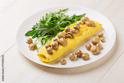 French three eggs omelette with mushrooms, arugula for a breakfast on a white plate on wooden background. Low carb diet.