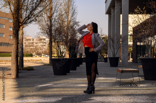 Confident woman in a red top and grey blazer outdoors.