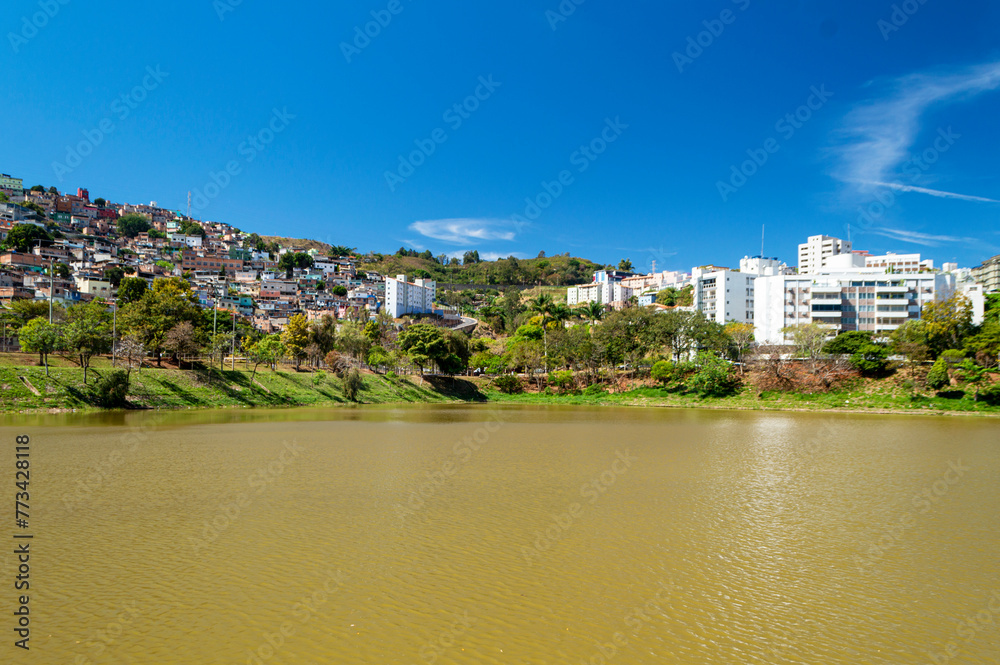 Residential houses in a favela on the edge of a lake with many trees. Blue sky with clouds. City of Belo Horizonte. Brazil