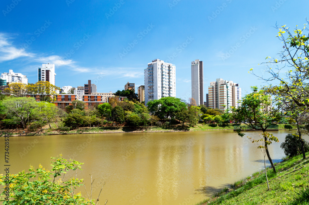 Residential buildings on the edge of a lake with many trees. Blue sky with clouds. City of Belo Horizonte. Brazil