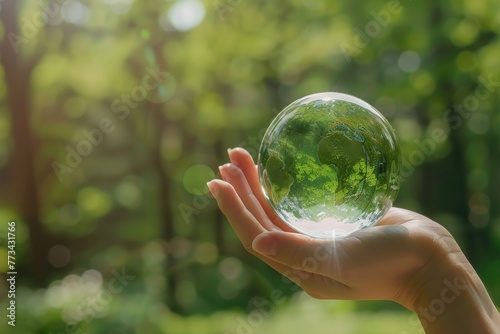Abstract human hands holding glass globe with green earth and natural forest landscape on blurred background