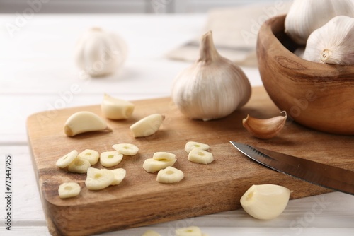 Aromatic cut garlic, cloves and bulbs on white wooden table, closeup