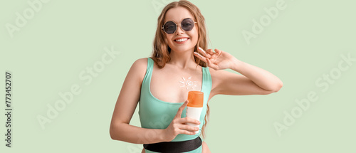 Beautiful young woman with sunscreen cream on green background © Pixel-Shot