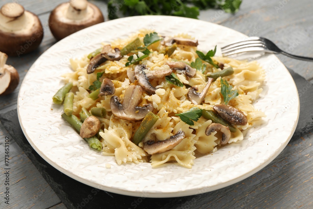 Vegetarian pasta with mushrooms, parsley, string beans and cheese on grey wooden table, closeup