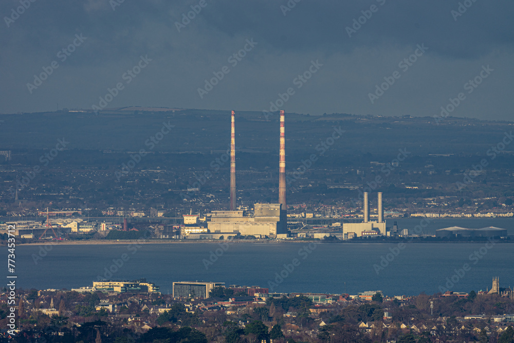 “Vista Industrial al Atardecer”. La foto captura una zona industrial con altas chimeneas destacando contra un vasto paisaje.