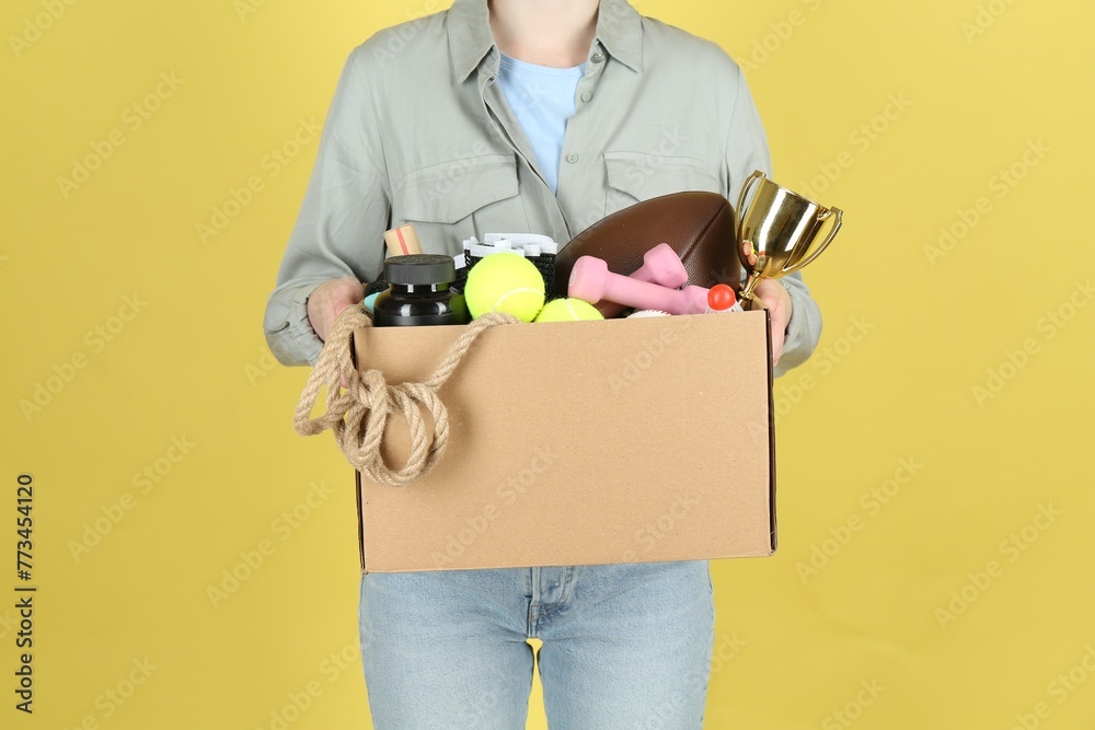 Fototapeta premium Woman holding box of unwanted stuff on yellow background, closeup