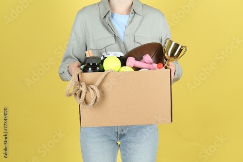 Woman holding box of unwanted stuff on yellow background, closeup