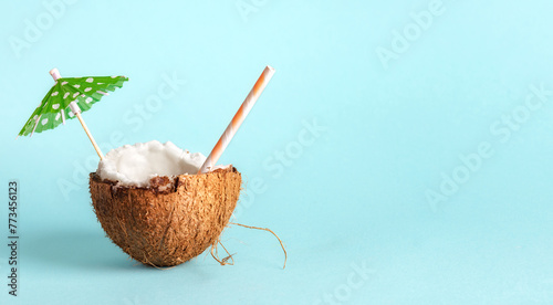 Half of a coconut with a sun umbrella and cocktail straw on a blue background with copy space. Creative concept summer beach holiday