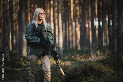 Beautiful military girl with a modern AK 12 suppressed rifle in the forest at war.