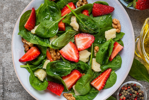 Healthy summer salad with spinach, strawberries, parmesan cheese, walnuts and olive oil in a plate. Top view. Delicious vegetarian food for lunch