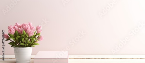 Pink flowers are displayed in a vase placed next to a book on a table surface photo
