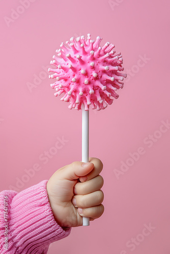 Child's hand grips lollipop shaped like a corona virus on pink background. Minimal concept of innocence in times of health crisis, pandemic, epidemic, spread infection, immunity.